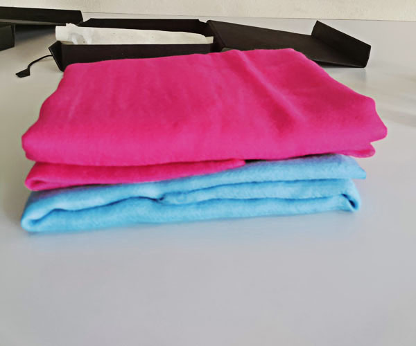 A hot pink featherlight cashmere scarf stacked on top of a baby blue featherlight cashmere scarf for packaging.