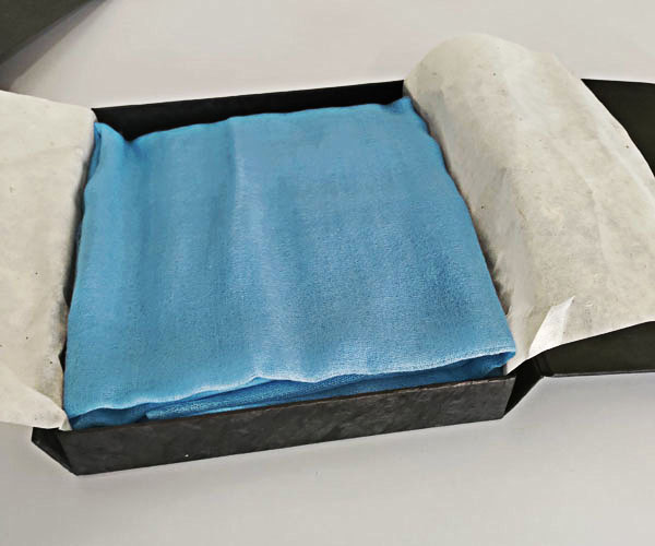 A baby blue featherlight cashmere scarf wrapped in a hand-made tissue and kept in a hard-covered paper box for shipping.